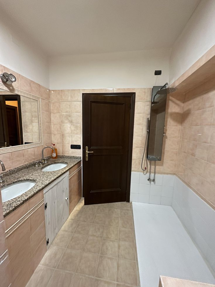 Bagno spazioso e ben illuminato con lavabo doppio, doccia e vasca. Elementi curati e pavimento in ceramica chiara.