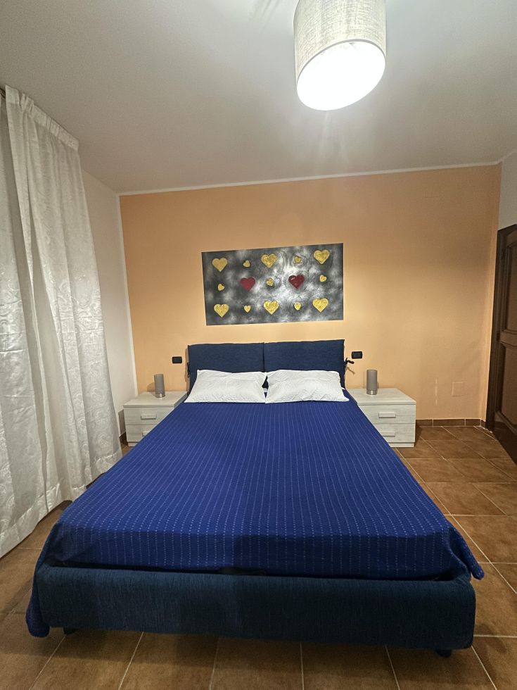 Camera luminosa e confortevole con letto matrimoniale, arredi semplici e una finestra che offre una piacevole illuminazione.