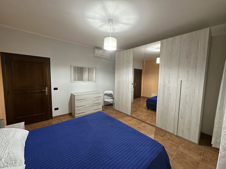 Camera semplice con letto matrimoniale e arredi funzionali, adatta per momenti di riposo.