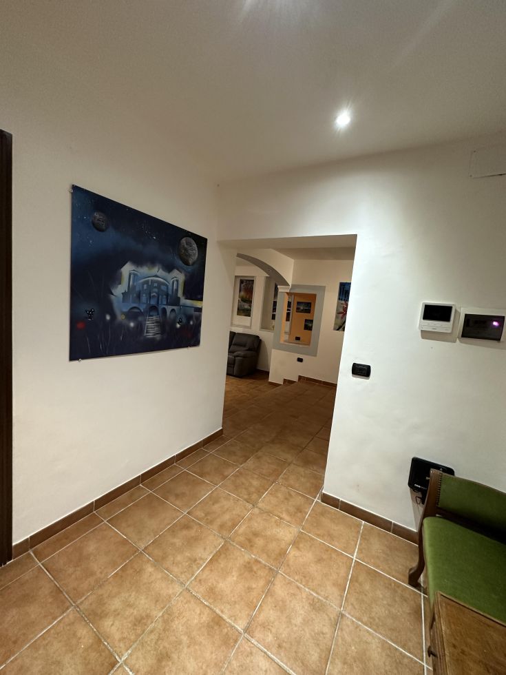 Un corridoio che porta a un soggiorno luminoso con un grande quadro appeso alla parete.