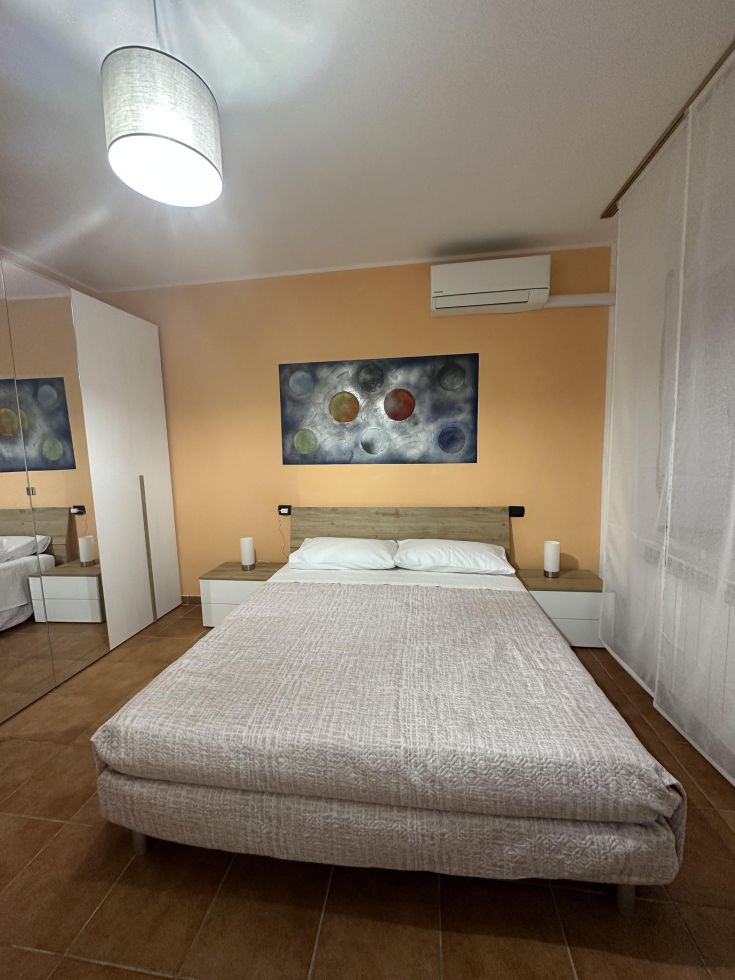 Camera matrimoniale spaziosa e luminosa, con arredi moderni e dettagli decorativi semplici sulle pareti.