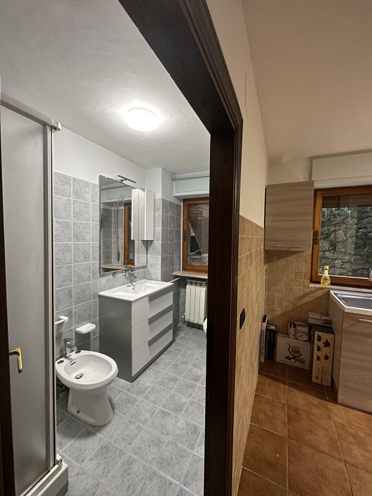 Un bagno con piastrelle grigie, dotato di specchio e lavabo, illuminato da luci soft.