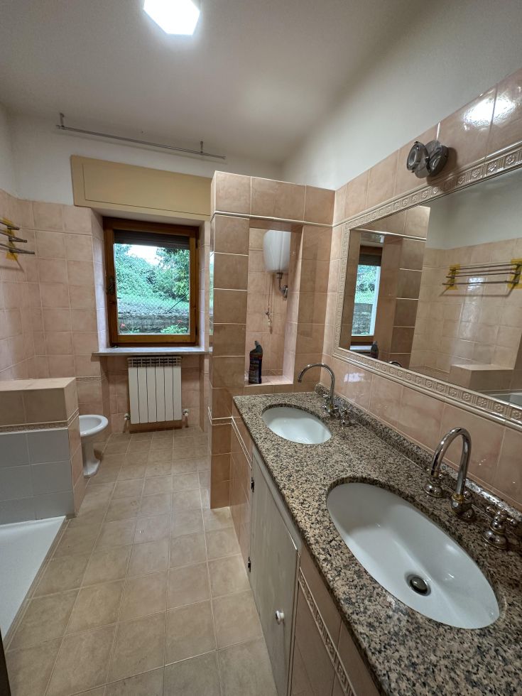 Bagno con doppio lavandino e doccia, arredato con piastrelle chiare e accessori semplici.