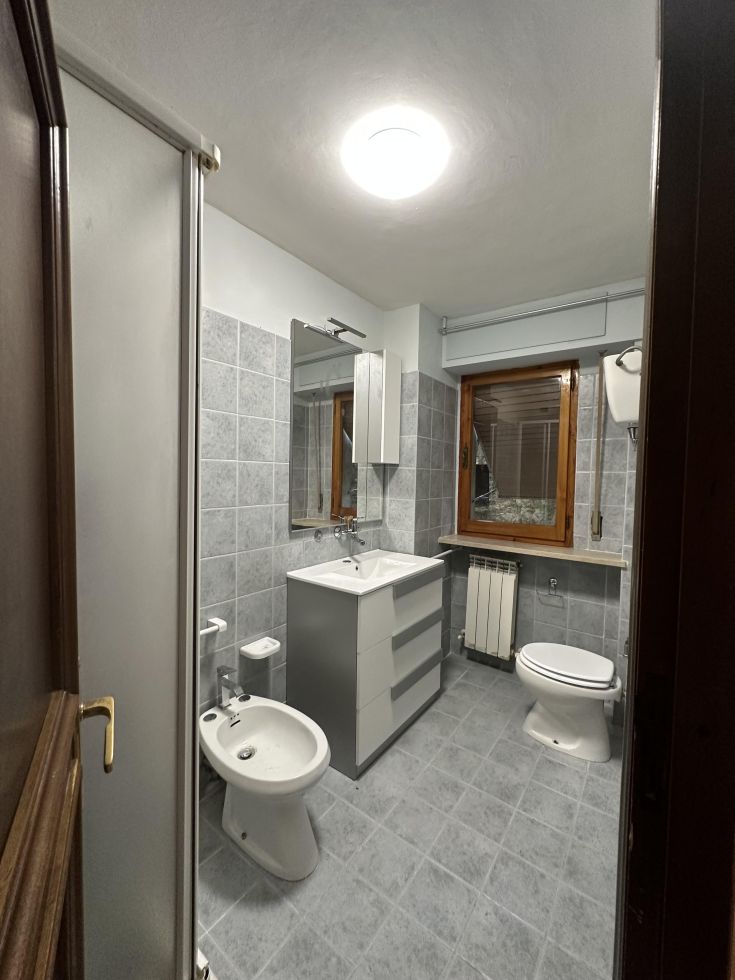 Un bagno contemporaneo con piastrelle grigie, un lavabo semplice e una finestra che porta luce all'interno.