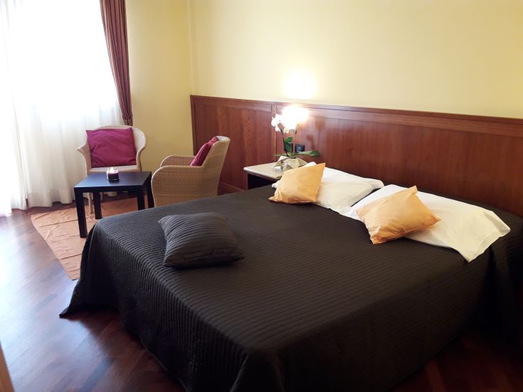 Cozy hotel room with a double bed, armchair, and bright scenic view.