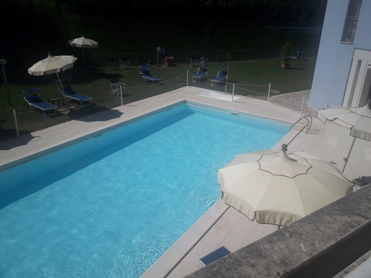 Zone de la piscine d'un hôtel situé près d'un lac, entourée de verdure.