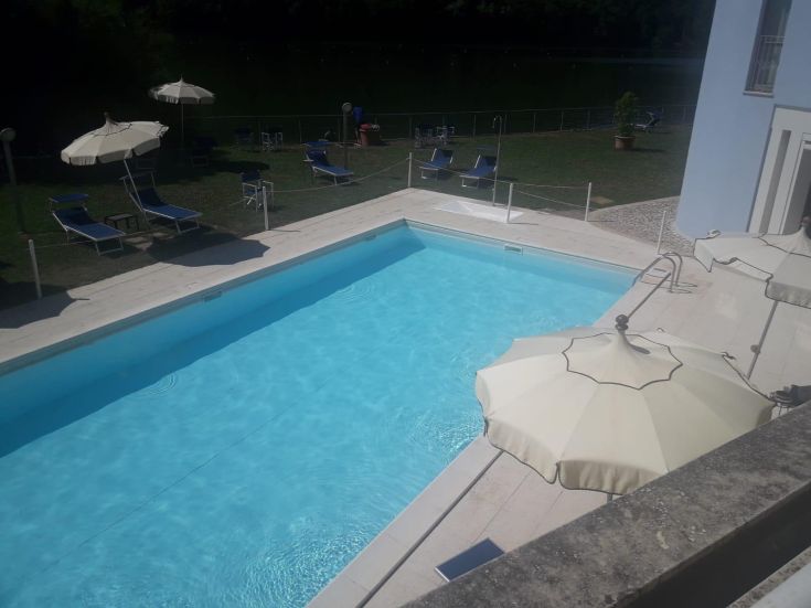 Hotel pool area located near a lake, surrounded by lush greenery.
