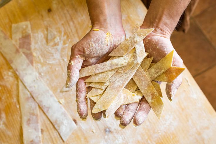 Mani che lavorano la pasta fresca, pronta per essere cotta e condivisa secondo la tradizione.