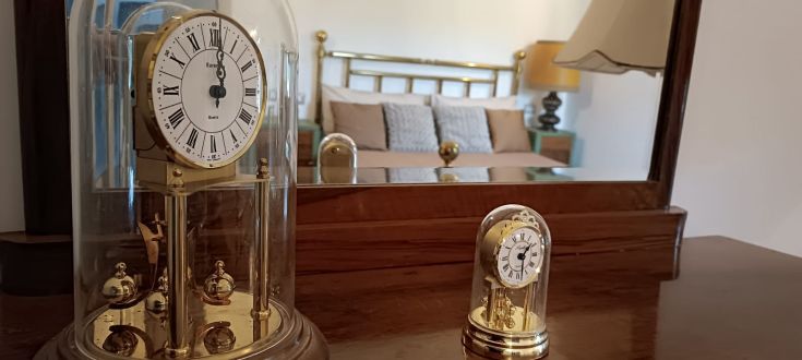 Un orologio da tavolo in una camera da letto confortevole, caratterizzato da dettagli dorati e un riflesso nello specchio.