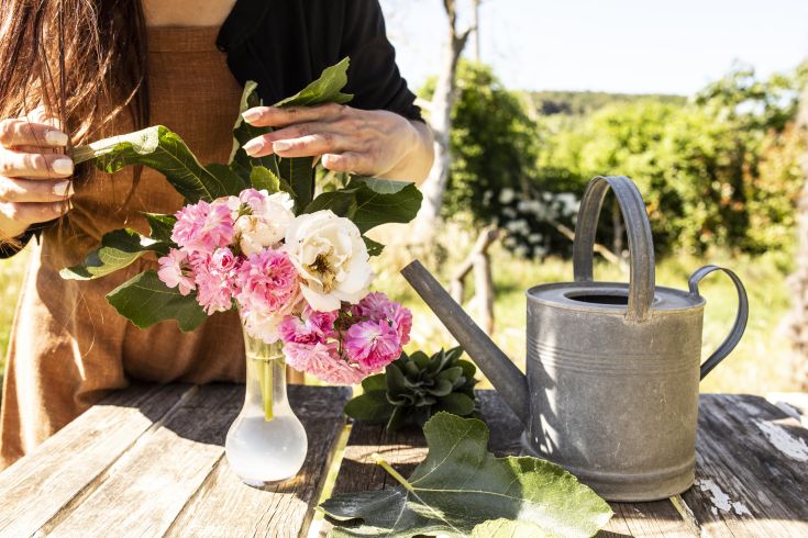 Composizione di fiori freschi con un annaffiatoio, immersi in un contesto naturale semplice.
