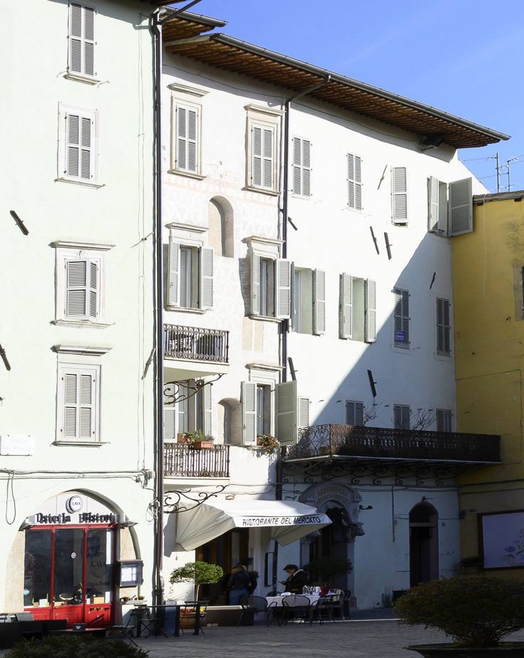 Bâtiment traditionnel avec des restaurants au rez-de-chaussée et des balcons décorés, situé dans une place animée.