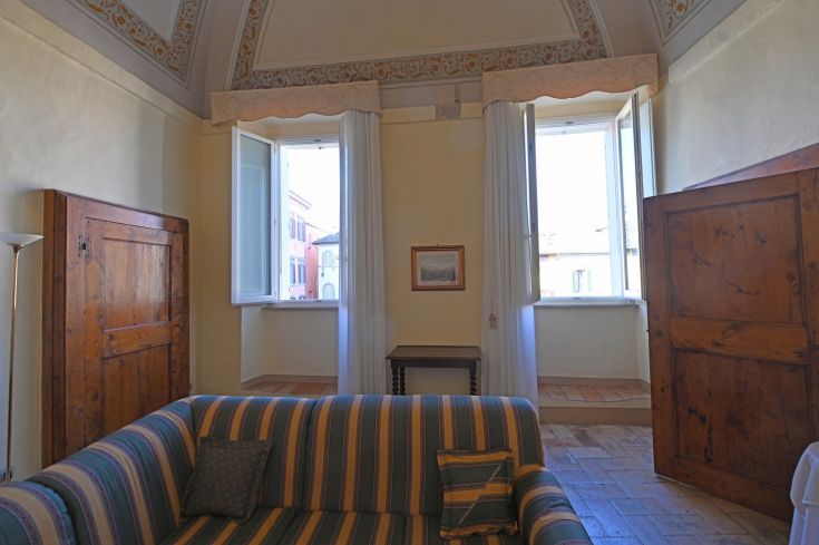 Élégant appartement historique à Spoleto avec des décorations murales et des fenêtres donnant sur une place.