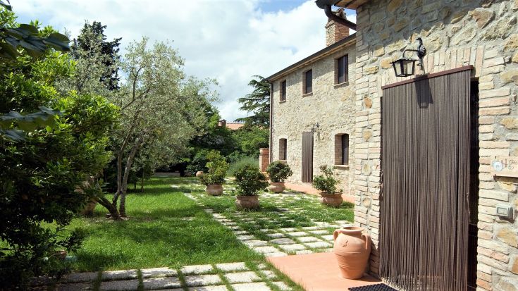 A farm stay surrounded by the Umbrian countryside, featuring a stone building and well-maintained gardens.
