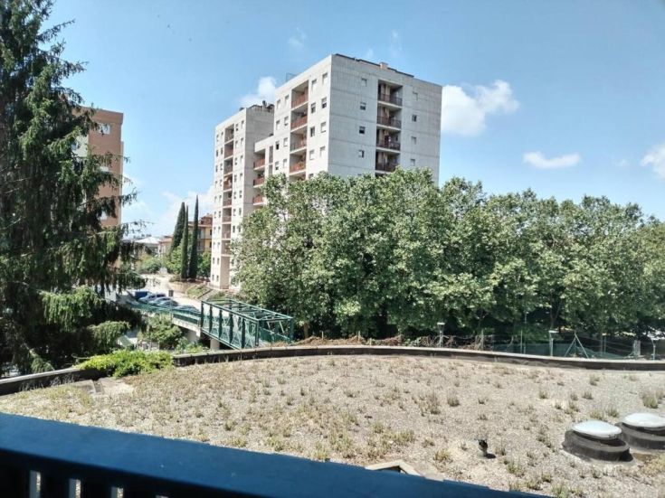 Una scena che ritrae edifici residenziali circondati da alberi e aree verdi, sotto un cielo limpido.