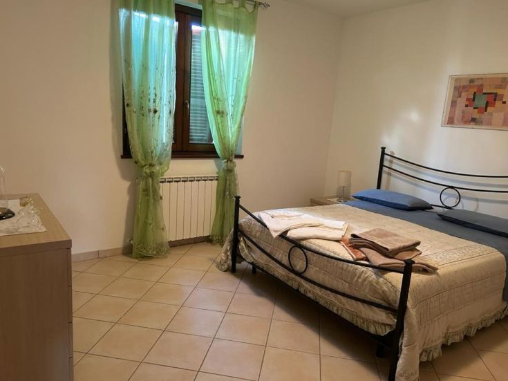 Bright room with beds, green linens, and curtains, creating a simple and relaxing atmosphere.