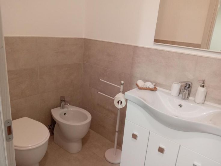 Un bagno minimalista con piastrelle chiare, lavabo semplice e bidet. Ambiente ordinato e luminoso.