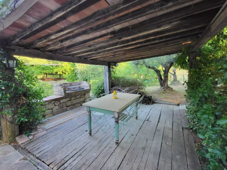 An outdoor area with a table and barbecue surrounded by nature.