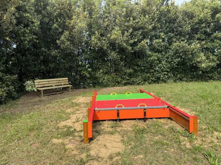 Outdoor children's play area surrounded by greenery, featuring a bench for relaxation.