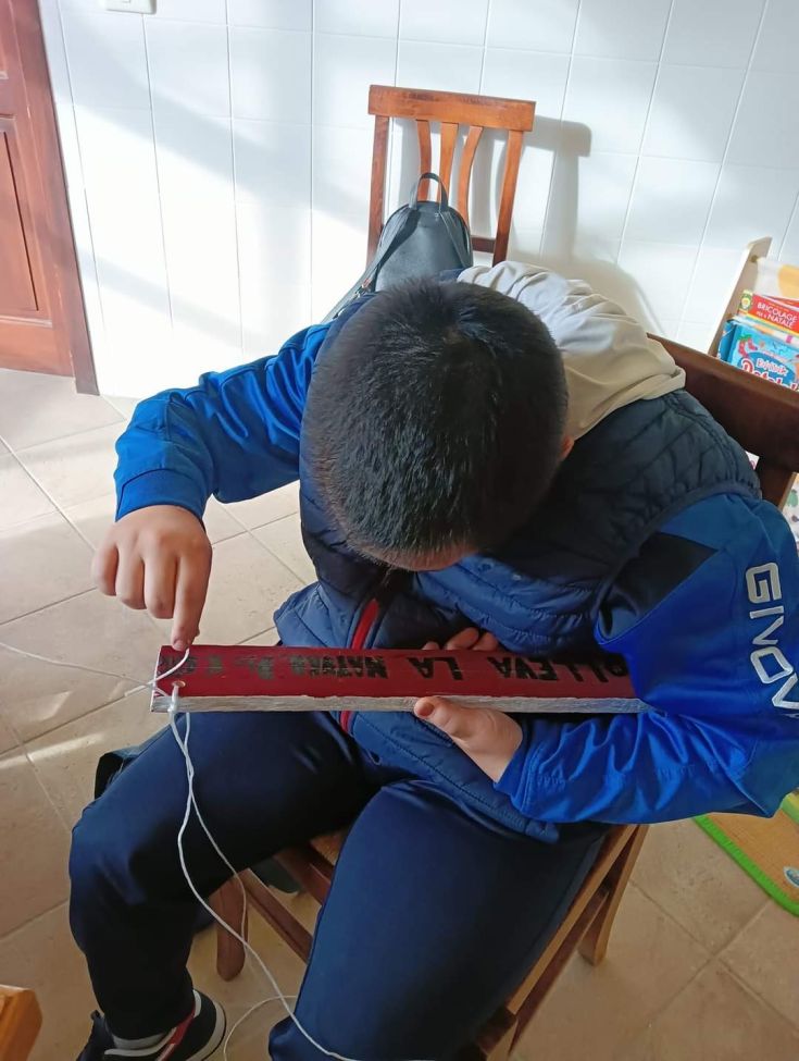 A young person works on a creative project, holding an object while sitting on a chair.