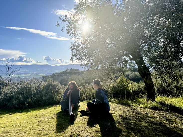 Two people relax in nature under a tree, enjoying a beautiful view of the surrounding landscape.