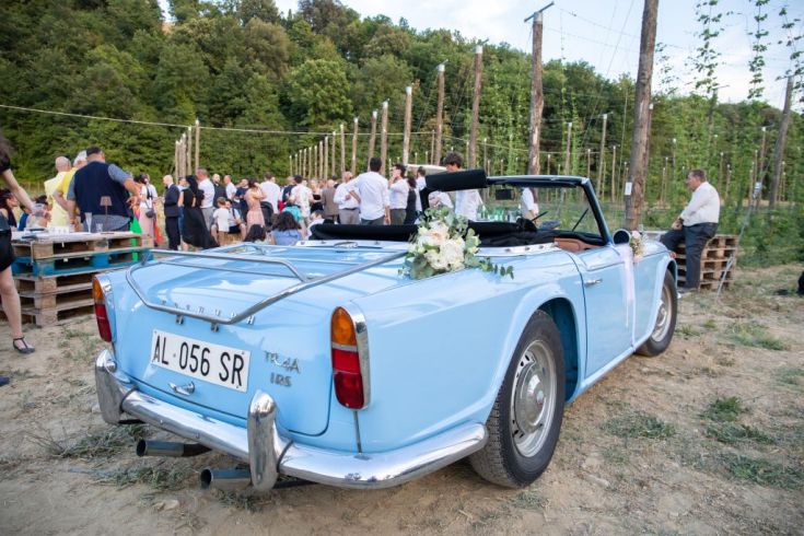 Un'auto d'epoca blu decorata con fiori esposta a un evento all'aperto, circondata da persone e attività conviviali.