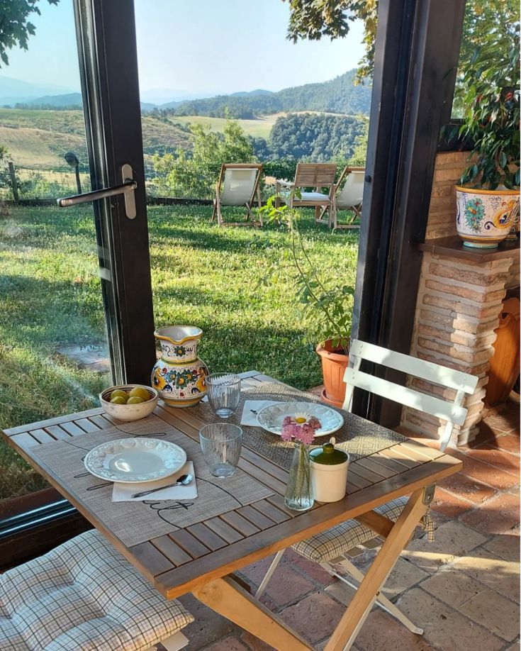 Un tavolo allestito per la colazione immerso nella natura, circondato da colline verdi.