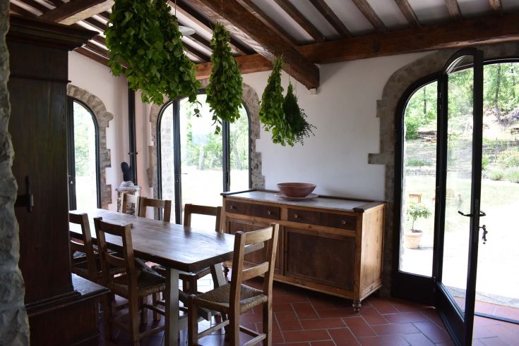 Ambiente interno ben illuminato con un tavolo in legno e piante aromatiche sospese, perfetto per momenti di incontro e socializzazione.