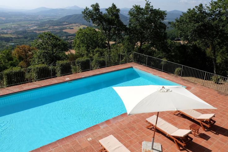 Panorama da una terrazza con piscina, circondata da alberi e verdi colline.