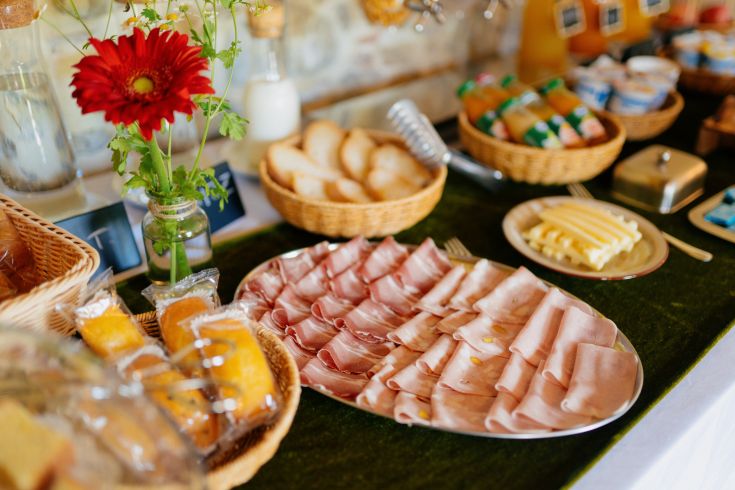 Un tavolo imbandito con affettati, formaggi, pane e qualche decorazione floreale, perfetto per una colazione tranquilla.