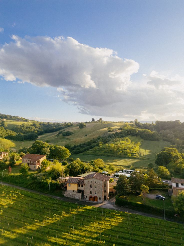 Un'ampia scena estiva delle colline umbre, caratterizzata da vegetazione lussureggiante e abitazioni in pietra.