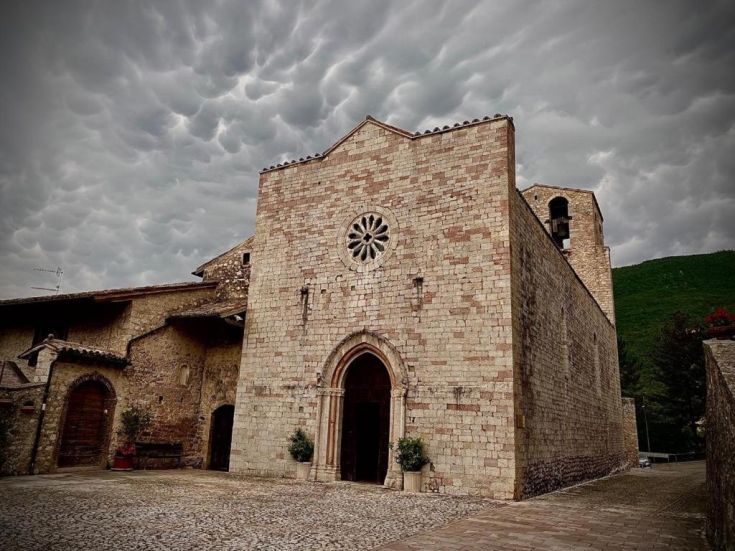 Szene einer mittelalterlichen Kirche in einem ruhigen Dorf unter einem bewölkten Himmel.