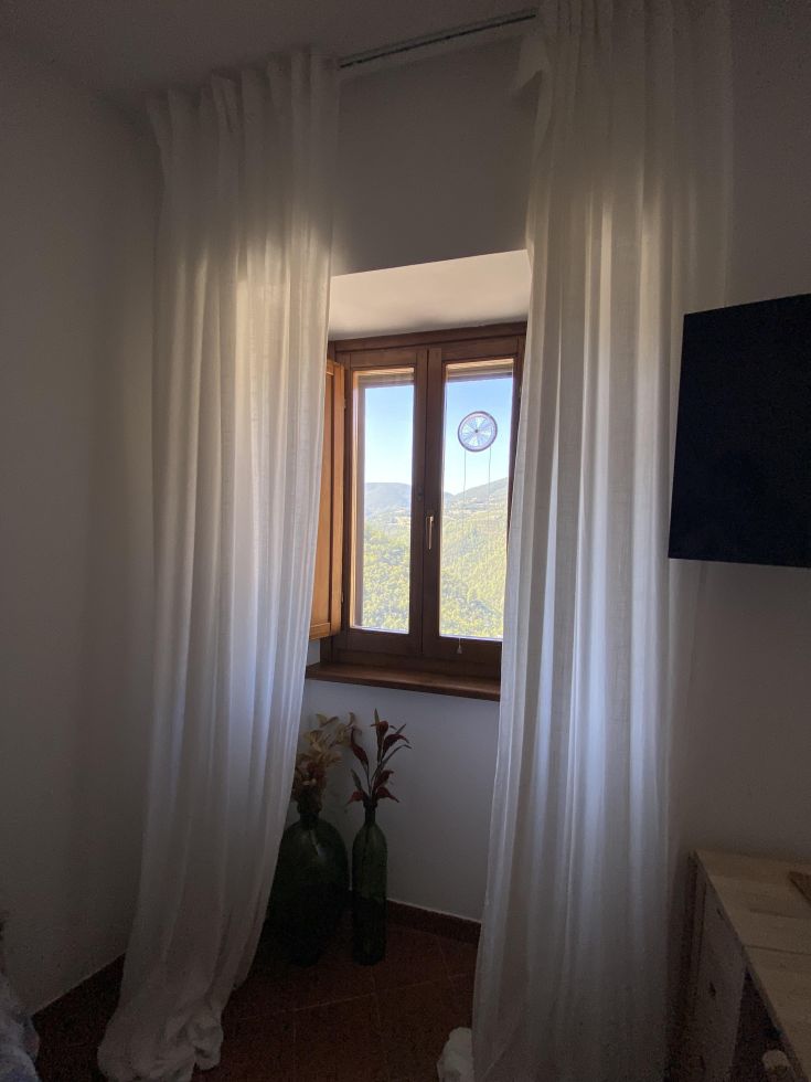 Ein komfortables Zimmer mit weißen Vorhängen und Blick auf die Berge, in einem historischen Dorf gelegen.