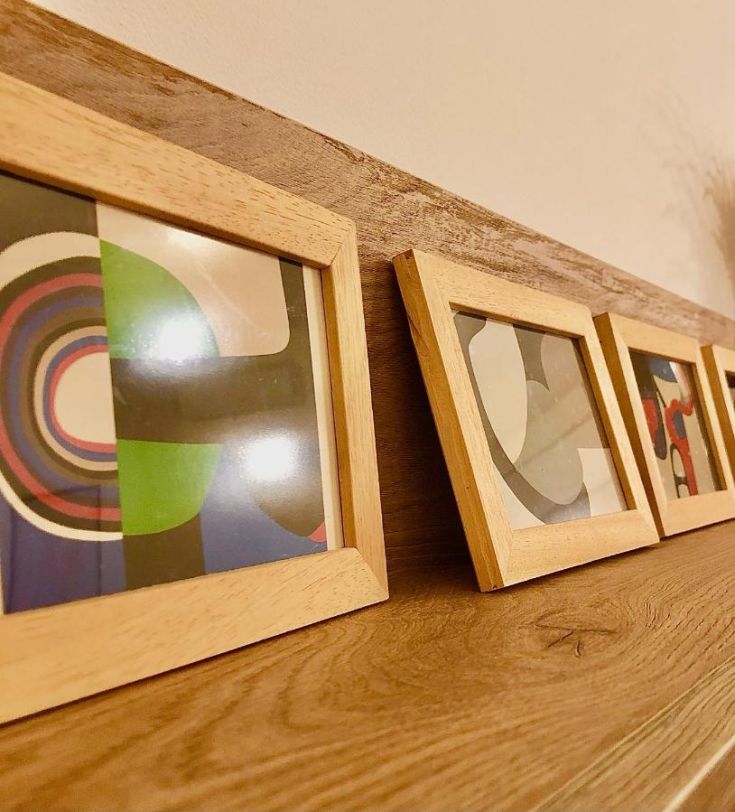 Four wooden frames holding modern images on a wooden shelf in a minimalist environment.