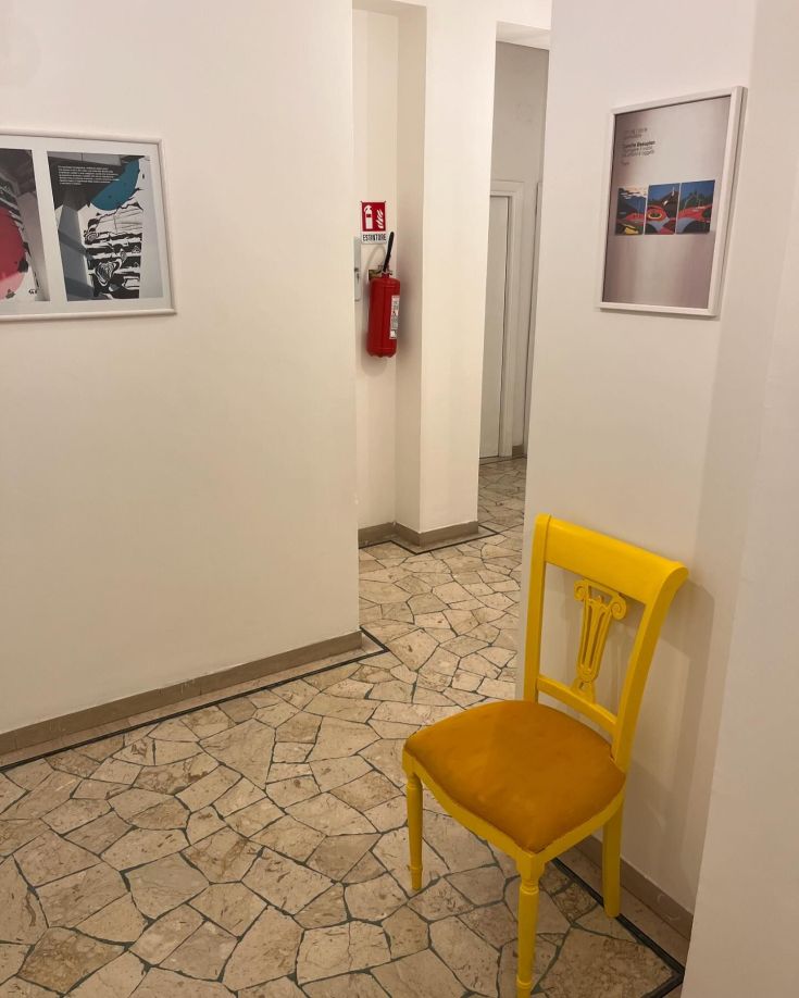 A simple corner featuring a yellow chair that adds a pop of color to a modern decorated hallway.