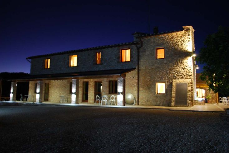 Ein beleuchteter Steinbauernhof am Abend, eingebettet in eine ruhige Umgebung.