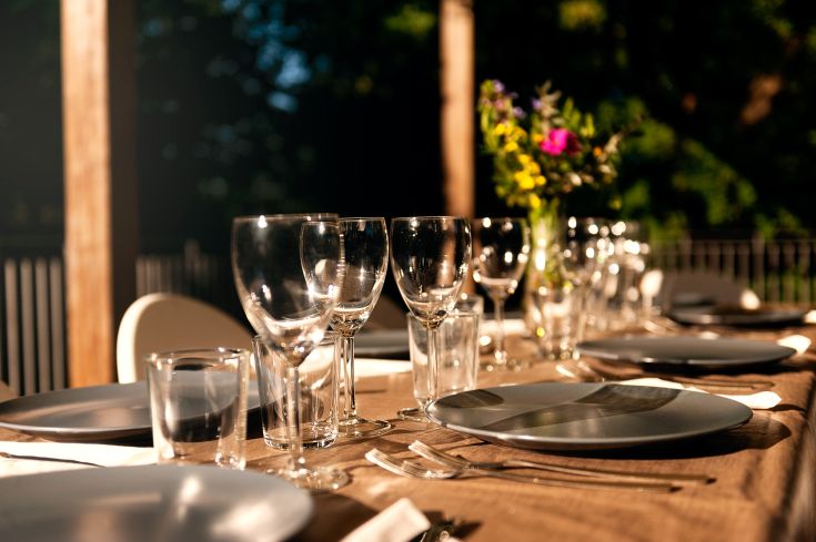 Tisch im Freien mit Geschirr und Dekorationen, bereit für ein Essen mit Freunden.