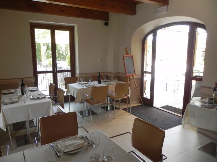 Innenansicht eines Restaurants mit gedeckten Tischen für Gäste und Blick auf einen Garten.