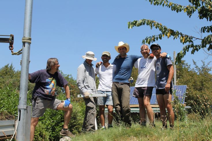 Eine Gruppe lächelnder Menschen versammeln sich im Freien unter einem klaren blauen Himmel und genießen einen Moment des Beisammenseins.