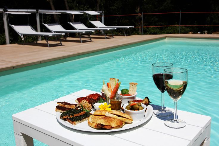 Ein einfacher Tisch mit leckeren Gerichten und Weinen neben einem sauberen Pool.