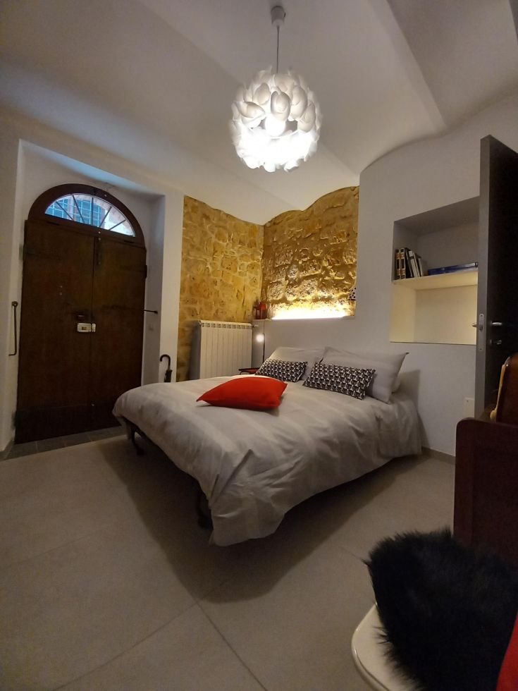 Camera semplice con letto matrimoniale e mobili essenziali, situata in un edificio storico.