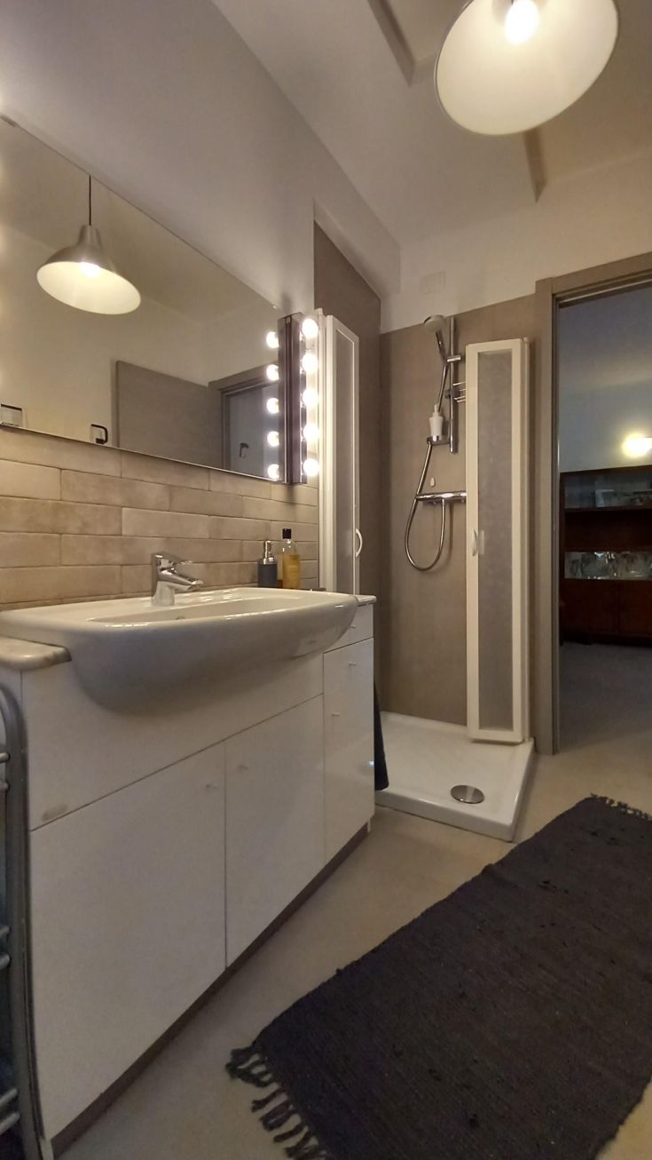 Un bagno arredato in stile semplice, dotato di lavabo, doccia e specchi. Buona distribuzione della luce e materiali funzionali.