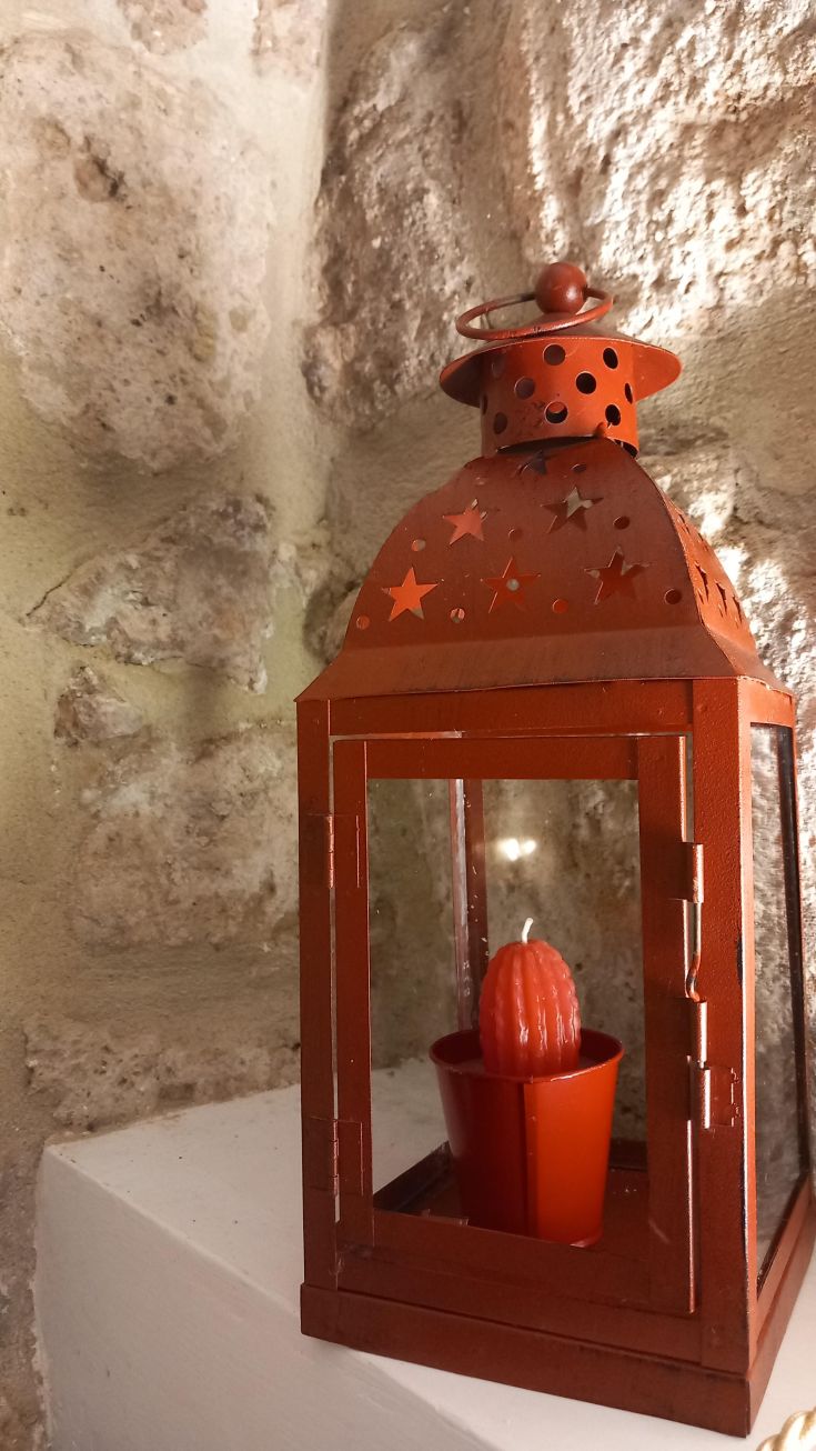 Lanterna rossa decorativa con candela a forma di cactus, situata in un ambiente semplice e rustico.