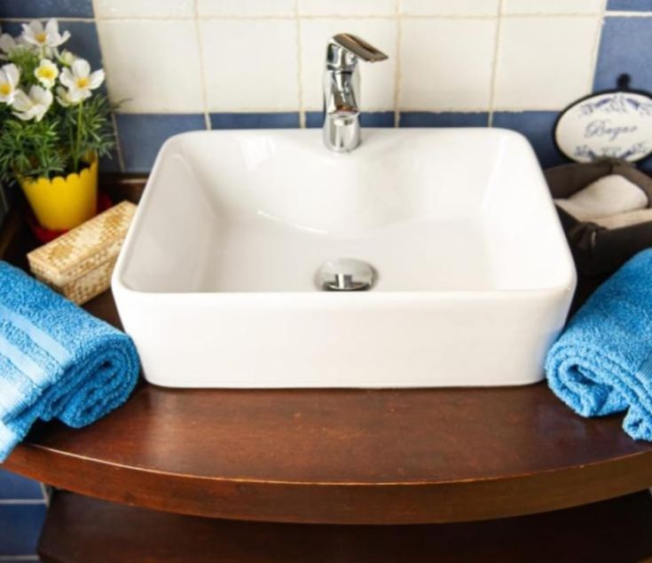 Ein modernes, schlichtes Waschbecken in einem gepflegten Bad, mit blauen Handtüchern und einigen dekorativen Blumen.