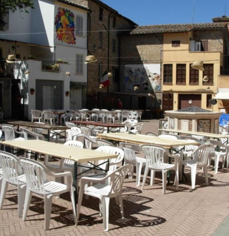Ein friedlicher Platz mit weißen Tischen und Stühlen, typisch für ein mittelalterliches Dorf in Umbrien.