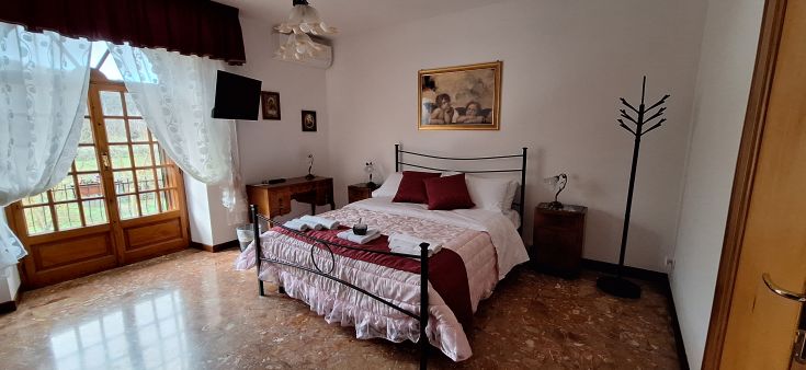 Camera confortevole con letto matrimoniale, affacciata su giardini e recante elementi semplici per un soggiorno tranquillo.