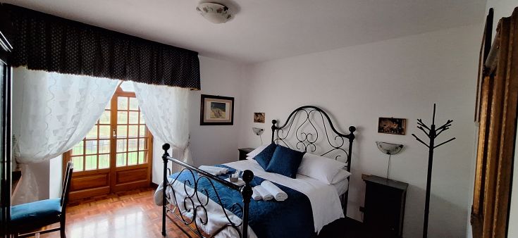 Camera semplice con letto matrimoniale e panorama su un paesaggio naturale.