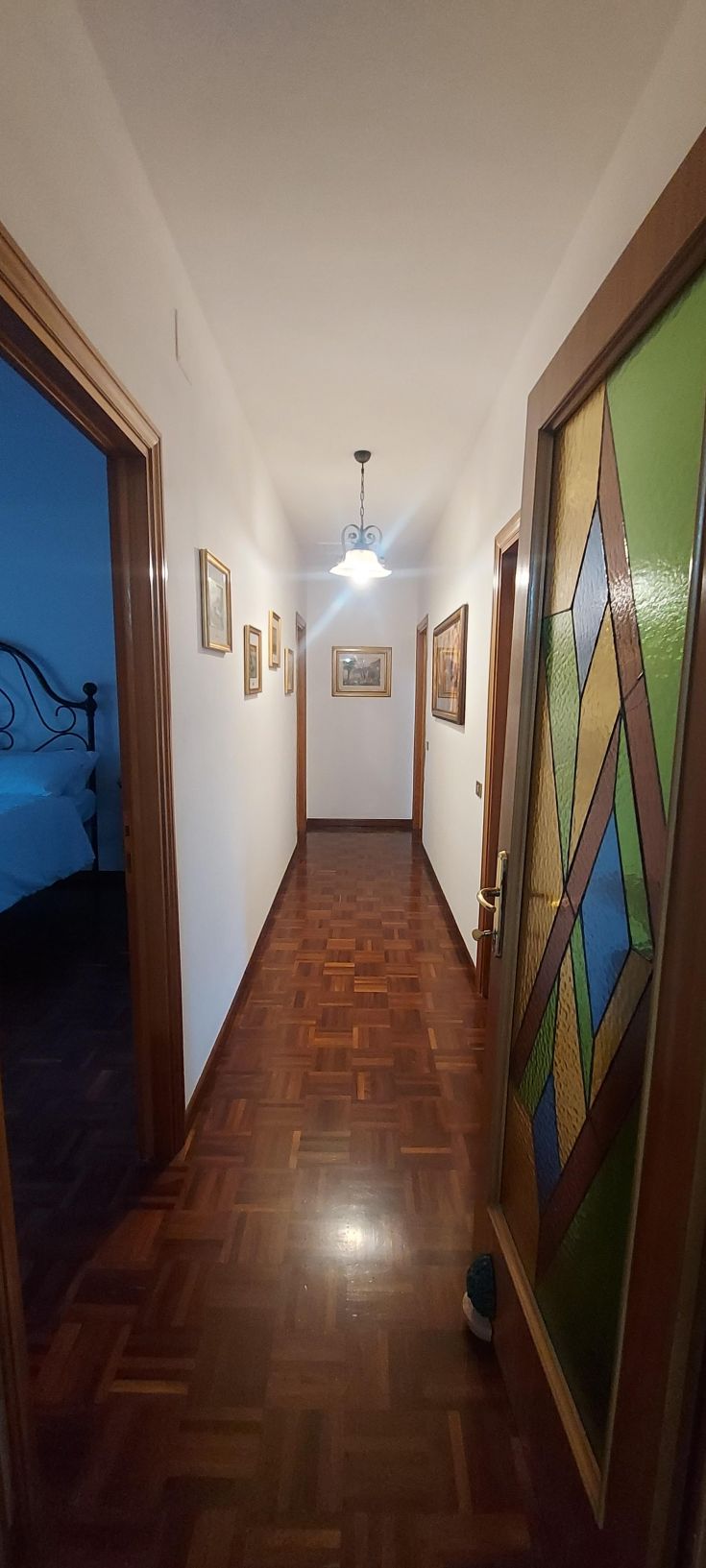 Un corridoio luminoso con porte in legno e pavimento in legno chiaro. Alcuni quadri decorano le pareti.