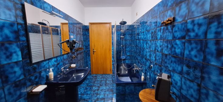 Bagno dai toni blu, dotato di vasca, doccia e grande specchio. Ambiente accogliente e ordinato.