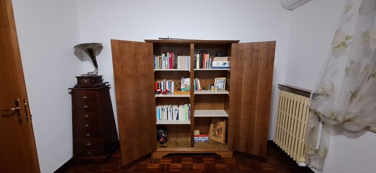 Armadio in legno aperto che espone libri e oggetti decorativi, situato in un ambiente semplice e ordinato.