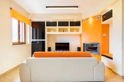 Un salotto semplice e confortevole, con colori caldi e una scena luminosa di finestre ampie.
